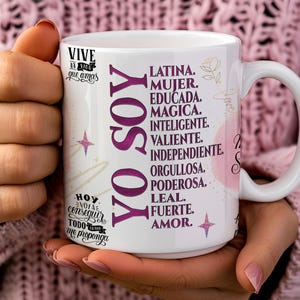 May include: White ceramic mug with a pink and purple design. The mug features the text "YO SOY" in large purple letters and a list of positive attributes in Spanish, including "Latina", "Mujer", "Educada", "Magica", "Inteligente", "Valiente", "Independiente", "Orgullosa", "Poderosa", "Leal", "Fuerte", and "Amor".