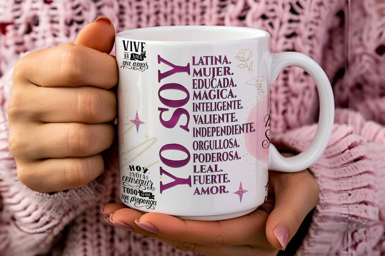 May include: White ceramic mug with a pink and purple design. The mug features the text "YO SOY" in large purple letters and a list of positive attributes in Spanish, including "Latina", "Mujer", "Educada", "Magica", "Inteligente", "Valiente", "Independiente", "Orgullosa", "Poderosa", "Leal", "Fuerte", and "Amor".