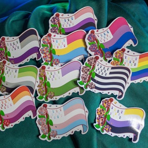 Peut inclure: Un ensemble de dix autocollants de drapeaux arc-en-ciel avec un motif floral. Chaque autocollant présente un drapeau arc-en-ciel différent, y compris les drapeaux transgenre, lesbien, gay, bisexuel, pansexuel, asexuel et non binaire. Les autocollants sont imprimés sur du papier blanc et ont une finition brillante.