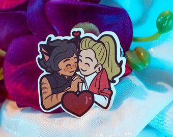 May include: A sticker featuring two cartoon characters, a cat-like person with brown fur and a woman with blonde hair, embracing with a red heart between them. The sticker is on a white background.