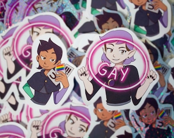 May include: Two stickers featuring cartoon characters from the animated series The Owl House. The first sticker features a character with purple hair and a green cloak holding a rainbow pride flag. The second sticker features a character with purple hair and a black shirt with the word "GAY" in pink neon letters.