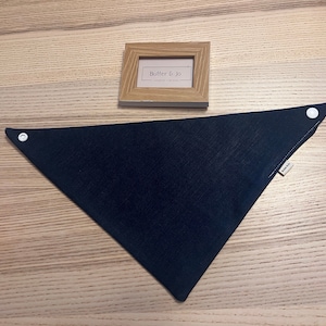 May include: A black triangular bandana with white snaps on the corners. The bandana has a small white label with the text "Butter & Jo" on it.