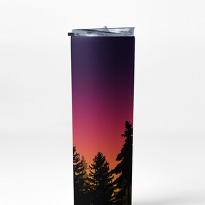 May include: A stainless steel tumbler with a black lid and a gradient design of purple, pink, orange, and yellow. The design features a silhouette of a forest at sunset.