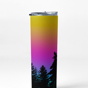 May include: A tall, stainless steel tumbler with a black lid. The tumbler has a gradient design with yellow, orange, pink, blue, and purple colors. The bottom of the tumbler features a silhouette of a forest.