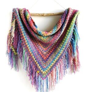 May include: A colorful crocheted triangular shawl with fringe. The shawl is made with a variety of bright colors, including red, orange, yellow, green, blue, and purple.