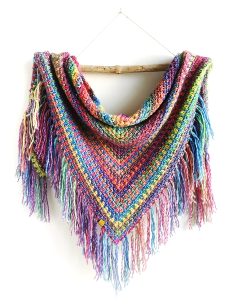 May include: A colorful crocheted triangular shawl with fringe. The shawl is made with a variety of bright colors, including red, orange, yellow, green, blue, and purple.