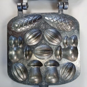 May include: A silver metal mold for making candy or chocolate. The mold has 10 different shapes, including mushrooms, nuts, and a long, thin shape.