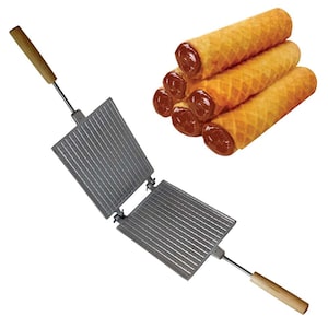 May include: A waffle iron with a wooden handle and two square metal plates. The plates have a waffle pattern and are hinged together. The iron is open, showing the inside of the plates. There are four waffle rolls filled with chocolate spread in the background.
