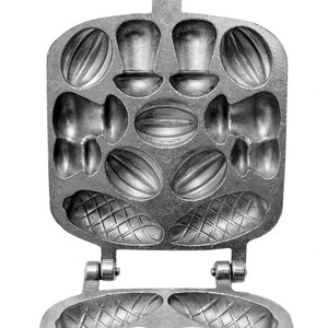 May include: A silver metal waffle iron with a hinged top and bottom. The top has multiple molds for making different shapes, including nuts, mushrooms, and a waffle pattern. The bottom has two large waffle molds.