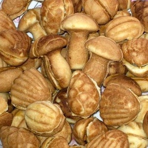 May include: A variety of small, brown, baked goods shaped like mushrooms and seashells. The baked goods are arranged in a pile on a white surface.