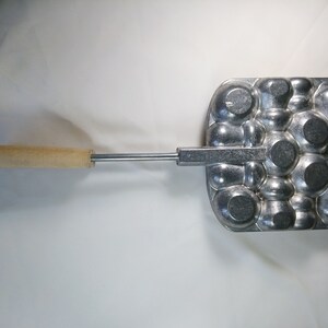 May include: A silver metal waffle iron with a wooden handle. The waffle iron has a pattern of round circles.