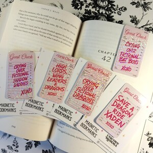 May include: Five rectangular magnetic bookmarks with a pink guest check design and holographic finish. Each bookmark features red text including phrases like Crying Over Fictional Bat Boys, High Lords, Wing Leaders & Dragons, and Save A Dragon Ride Xaden.