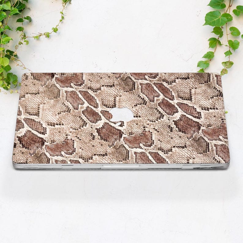 Puede incluir: Una funda para port&aacute;til con un dise&ntilde;o de piel de serpiente en tonos marr&oacute;n, beige y crema. La funda tiene un recorte para el logotipo de Apple y es de forma rectangular. El dise&ntilde;o imita la apariencia de la piel de reptil.
