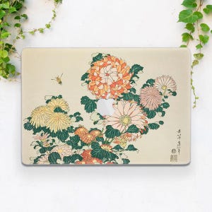 Könnte beinhalten: Laptop-Hülle mit floralem Design aus orangefarbenen, gelben und rosa Chrysanthemen, grünen Blättern und einer kleinen Biene. Das Design ist vor einem beigefarbenen Hintergrund mit japanischem Text und einem Siegel.