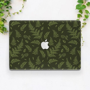 Può includere: Una custodia per laptop con un motivo a foglie di felce in tonalità di verde su uno sfondo verde scuro. Il logo Apple è visibile al centro. La custodia è rettangolare e ha angoli arrotondati.