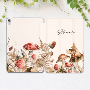 May include: A white iPad case with a watercolor design of mushrooms and ferns. The case has a flap that folds over the screen and has the name "Alexandra" written on it.