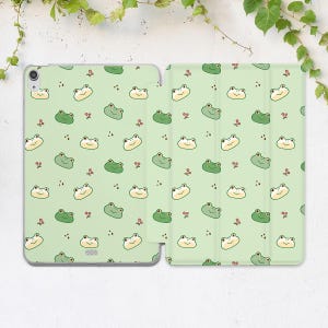 May include: A light green iPad case with a repeating pattern of cartoon frogs in green and cream colors, along with small red berry-like accents. The case is open, displaying the interior.