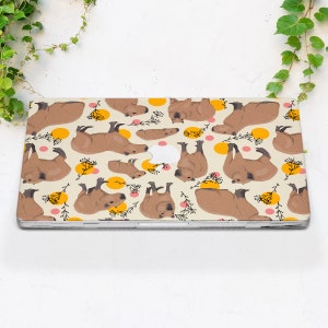 May include: A laptop skin with a repeating pattern of brown capybaras in various poses on a cream background with yellow and pink circles.