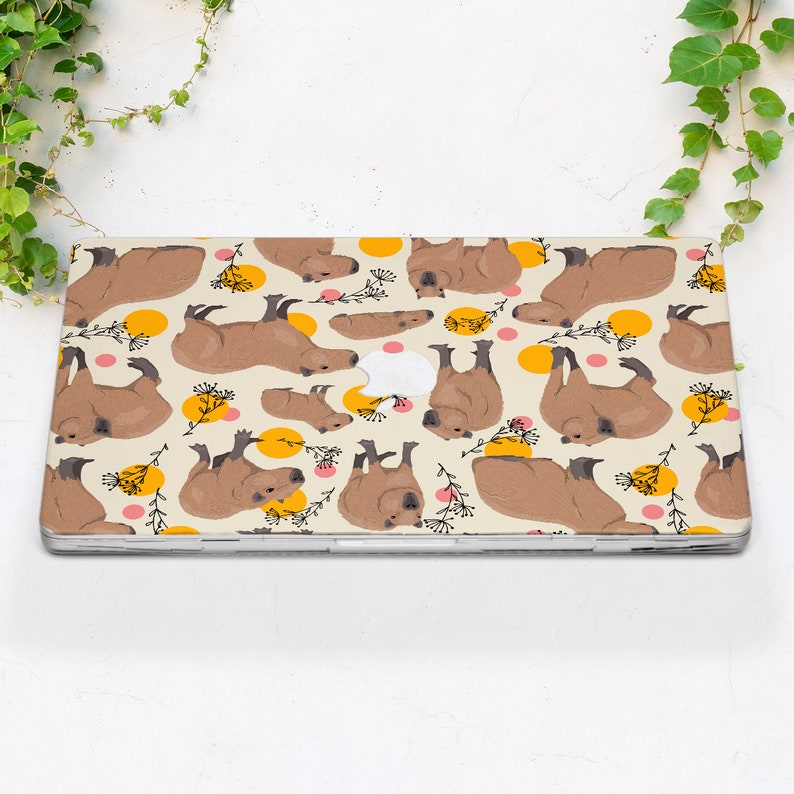 May include: A laptop skin with a repeating pattern of brown capybaras in various poses on a cream background with yellow and pink circles.