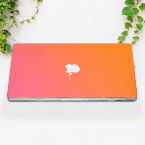 May include: A laptop computer with a pink to orange gradient color scheme. The Apple logo is visible on the lid.