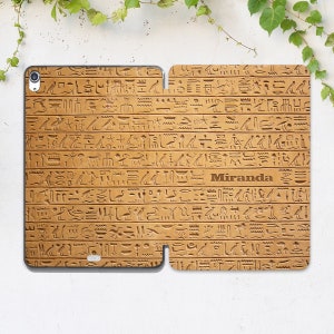 May include: A brown leather phone case featuring a pattern of ancient Egyptian hieroglyphs. The name "Miranda" is engraved on the case.