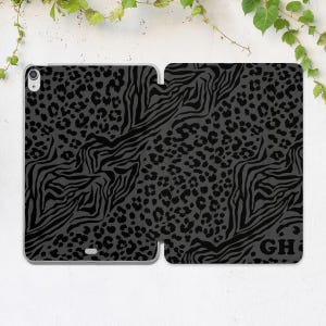 May include: A gray tablet case with a black animal print design. The case features a combination of leopard spots and zebra stripes. The initials "GH" are visible on the lower right corner of the case.
