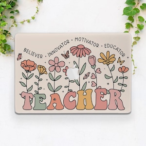 Può includere: Una custodia beige per laptop con un design floreale. Il design include la parola "TEACHER" in lettere retrò, fiori, farfalle e le parole "BELIEVER, INNOVATOR, MOTIVATOR, EDUCATOR".