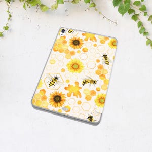 K&ouml;nnte beinhalten: Eine transparente Tablet-H&uuml;lle mit einem sich wiederholenden Muster aus gelben Sonnenblumen, Bienenwaben und Bienen. Das Design hat einen Aquarell-Effekt mit wei&szlig;em Hintergrund und einem gelben Farbtupfer. Die H&uuml;lle ist f&uuml;r ein Tablet konzipiert.