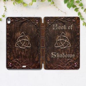 Peut inclure: Un livre relié en cuir marron avec un symbole triquetra doré et le texte "Book of Shadows" sur la couverture.