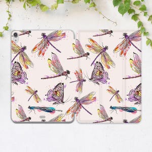 May include: A light pink tablet case featuring a repeating pattern of colorful dragonflies and butterflies. The insects are in shades of purple, yellow, and orange, with watercolor-style details. The case is open, showing the interior.
