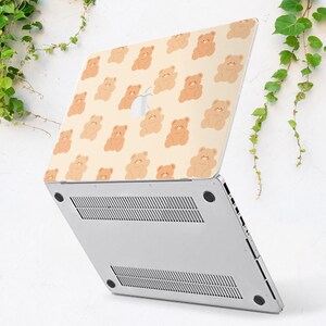 May include: A white laptop with a beige and brown teddy bear pattern on the lid. The laptop is closed and the bottom of the laptop is visible.