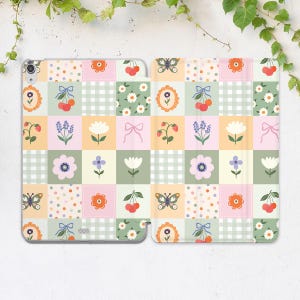 May include: A colorful tablet case with a patchwork design. The case features squares with floral, butterfly, and cherry patterns in pastel colors. The case is open, revealing the tablet screen.