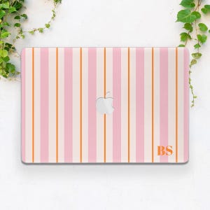 May include: A laptop skin featuring a vertical striped pattern in alternating shades of light pink, white, and thin orange lines. The center displays a silver Apple logo cutout, and the bottom right corner features the orange monogram letters BS.