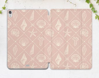 Può includere: Una custodia rosa per tablet con un motivo ripetuto di conchiglie bianche, stelle marine e fiocchi. Il design è ambientato su uno sfondo a griglia, creando un tema nautico. La custodia è aperta, mostrando il design interno ed esterno.
