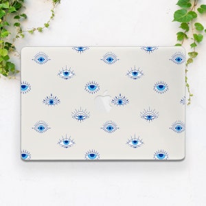 May include: A white laptop computer with a clear protective case featuring a repeating pattern of blue evil eyes. The eyes are stylized with dark blue outlines and white accents.