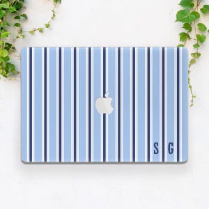 May include: A light blue laptop case with a vertical striped pattern in white and navy blue. The Apple logo is centered, and the initials "SG" are in the lower right corner. The case is rectangular and has a glossy finish.