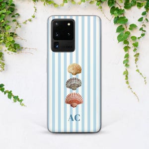 May include: A smartphone case featuring a vertical light blue and white striped pattern. The design includes three stacked seashells in shades of tan, gray, and reddish-brown, positioned above the capitalized blue letters AC centered at the bottom.