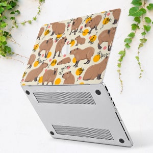May include: A laptop computer with a white background and a colorful design featuring capybaras, flowers, and yellow circles. The design is on the back of the laptop.