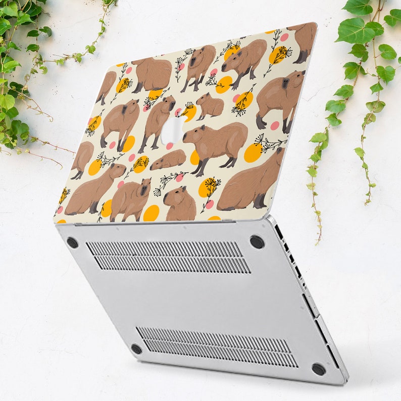May include: A laptop computer with a white background and a colorful design featuring capybaras, flowers, and yellow circles. The design is on the back of the laptop.