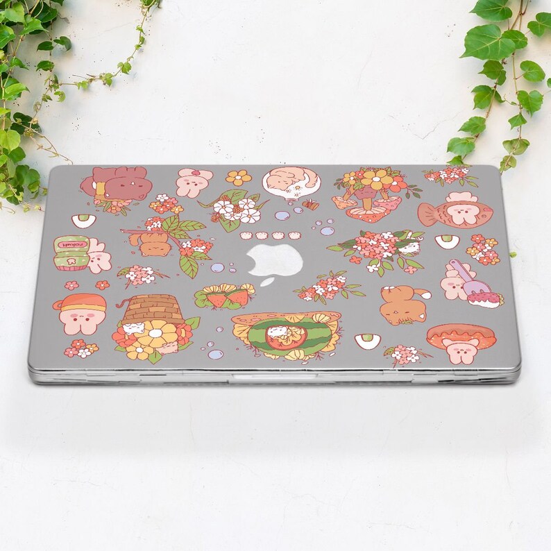 May include: A grey laptop with a variety of colourful stickers featuring cartoon animals, flowers, and food. The stickers are arranged in a random pattern across the laptop's surface.