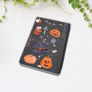 May include: Black Halloween-themed iPad case with a witch's hat, bats, pumpkins, and mushrooms. The case has a black and white striped flap.