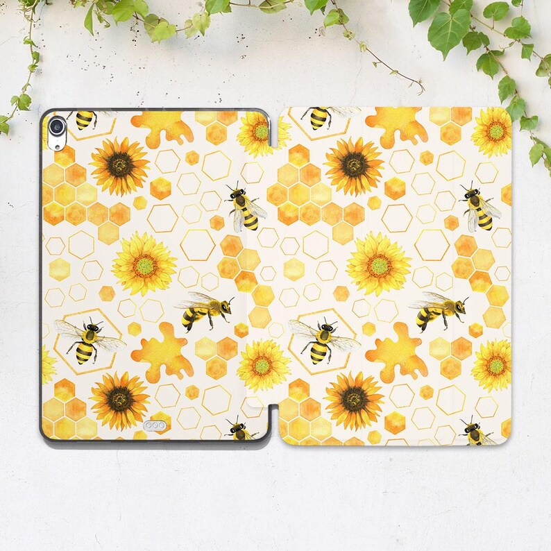 K&ouml;nnte beinhalten: Eine wei&szlig;e Tableth&uuml;lle mit einem sich wiederholenden Muster aus Sonnenblumen, Bienenwaben und Bienen. Das Design enth&auml;lt gelbe, goldene und schwarze Elemente. Die H&uuml;lle ist offen und zeigt das Innendesign und ist f&uuml;r ein Tablet geeignet.