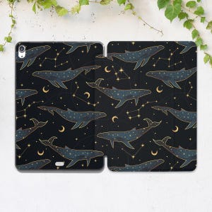 May include: A black tablet case with a repeating pattern of whales, constellations, and crescent moons in gold and blue. The design creates a celestial theme, suitable for protecting a tablet.