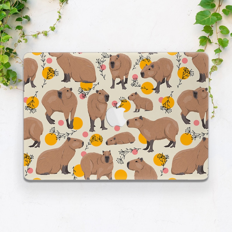 May include: A laptop skin with a repeating pattern of capybaras on a cream background. The capybaras are brown and are in various poses. The background is accented with yellow and pink circles and black floral designs.