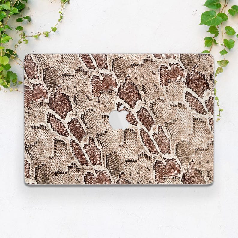Puede incluir: Una funda para port&aacute;til con un dise&ntilde;o de piel de serpiente en tonos marr&oacute;n, beige y beis. La funda tiene un recorte para el logotipo de Apple. Hay vides verdes en el fondo.