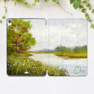 May include: An iPad case featuring a landscape painting of a river scene with trees and grassy banks. The artwork has a soft, impressionistic style with a muted color palette of greens, blues, and whites. The name "Chris" is written in cursive on the case.