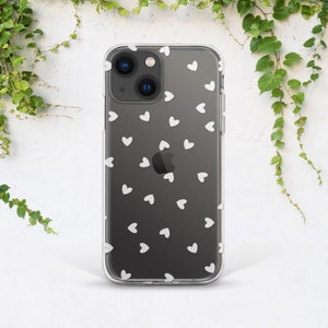 May include: Transparent phone case featuring a scattering of small white hearts. The case is on a black phone, with the heart pattern repeated. Green foliage is visible in the background.