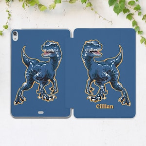 May include: A blue iPad case with a graphic of a blue dinosaur on each side. The case has the name "Cillian" printed on the bottom right side.