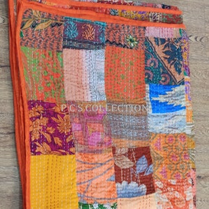 May include: A colourful patchwork quilt featuring squares of orange, yellow, purple, and blue fabrics. The quilt is hand-stitched with white thread and has an orange border. The text "PCS COLLECTION" is visible on the quilt's surface.