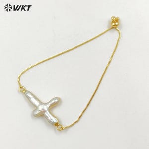 May include: A gold chain bracelet with a white pearl cross charm. The bracelet has an adjustable sliding clasp.